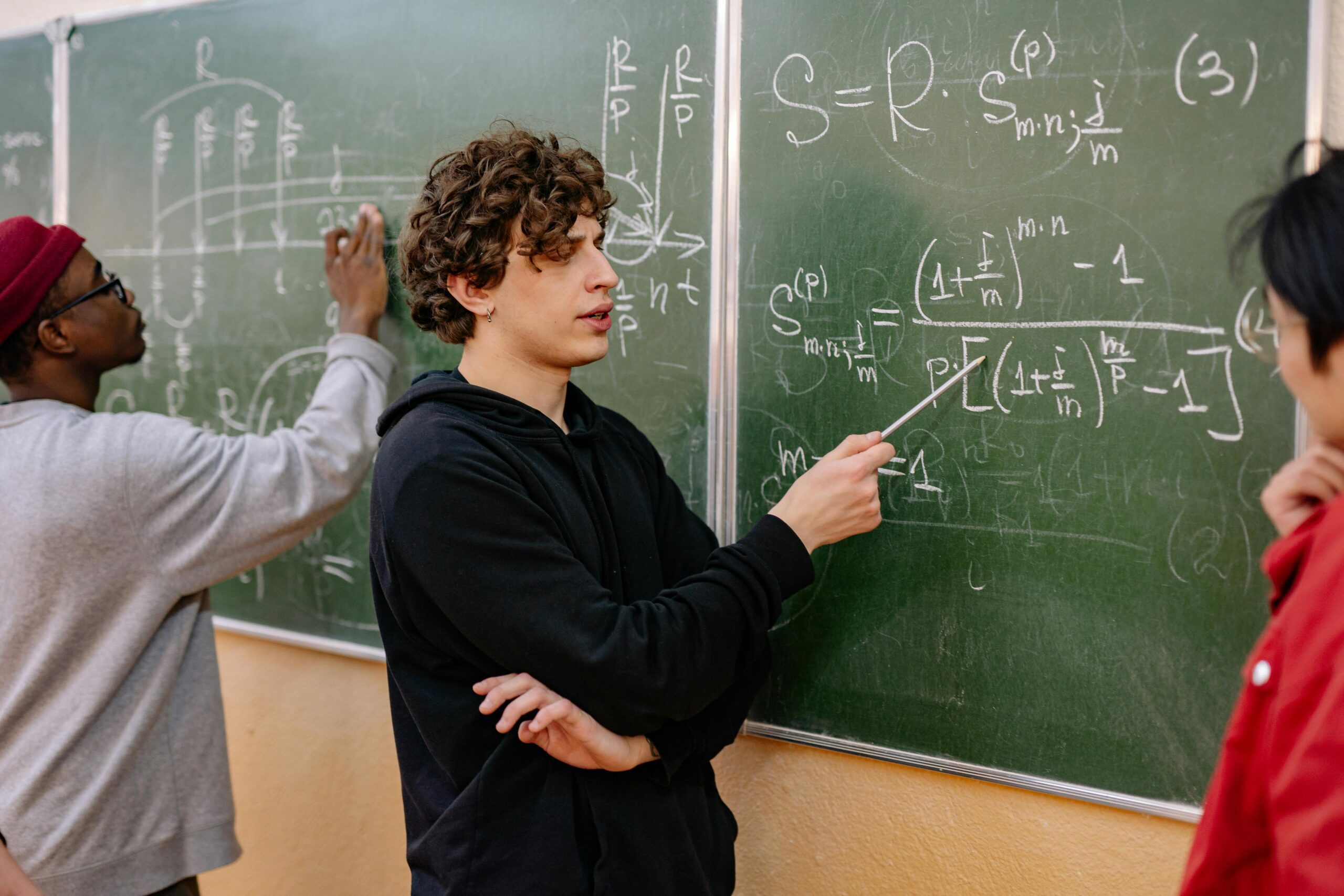 Group of students analyzing complex mathematical equations on a chalkboard in a classroom setting.