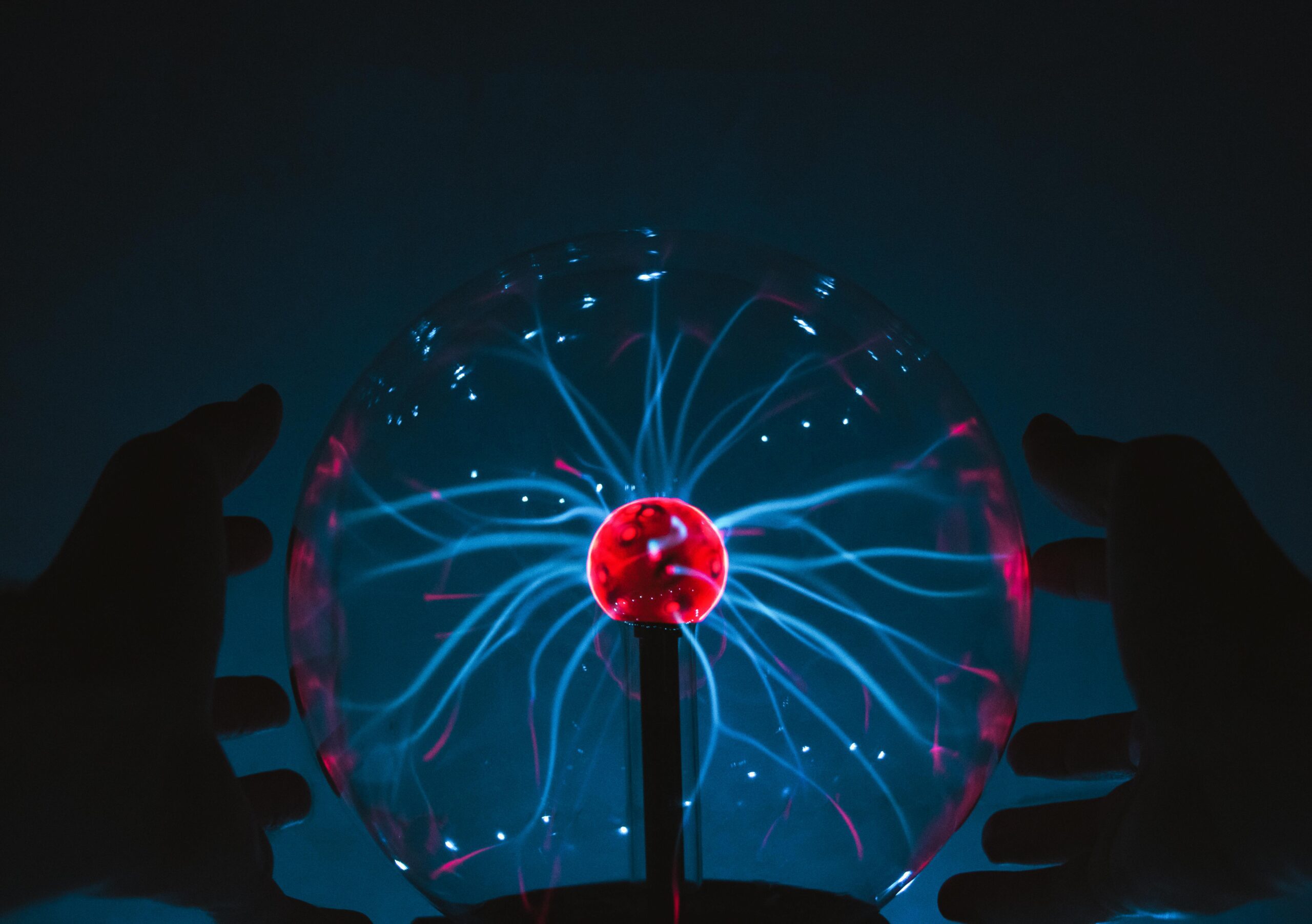 Close-up of hands around a glowing plasma ball emitting electric discharge.
